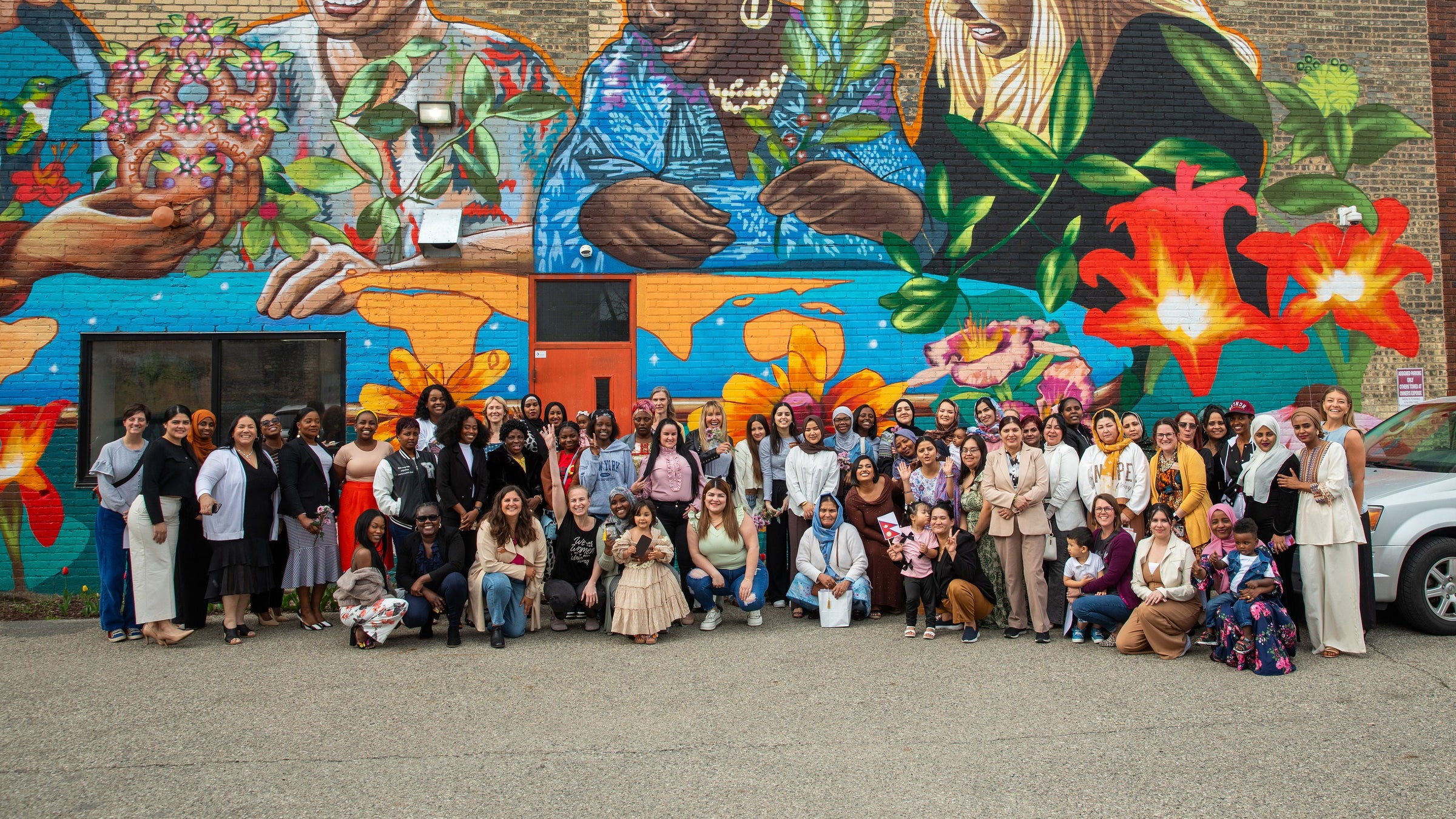 Group of people posing in front of a colorful mural of women and flowers.